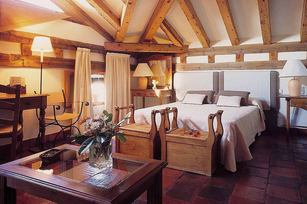 A cozy bedroom with a large bed, wooden furniture, and a rustic ceiling.