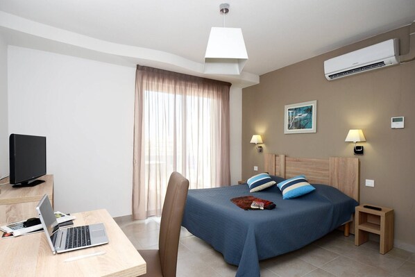 Habitación de hotel con una cama, un escritorio con una computadora portátil, un televisor y un aire acondicionado.