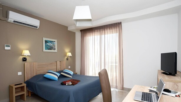 Habitación de hotel con cama, lámparas de noche, escritorio con una computadora portátil, televisor y ventana con cortinas.