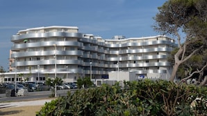 Un edificio residencial de varios pisos con balcones, un estacionamiento y cielo despejado.