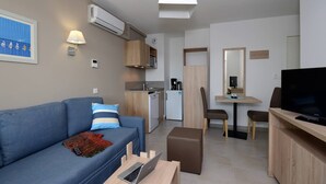 Un espacio habitable compacto con sofá, zona de comedor, kitchenette y televisor.