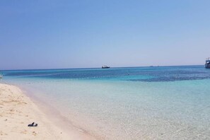 A beach with clear turquoise water, a boat in the distance, and a sandy shore. - Beautiful apartment near Port-Barcarès Beach (Le Barcares)
