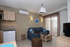 Una sala de estar moderna con un sofá, una mesa de centro, un televisor y una zona de cocina con lavavajillas.