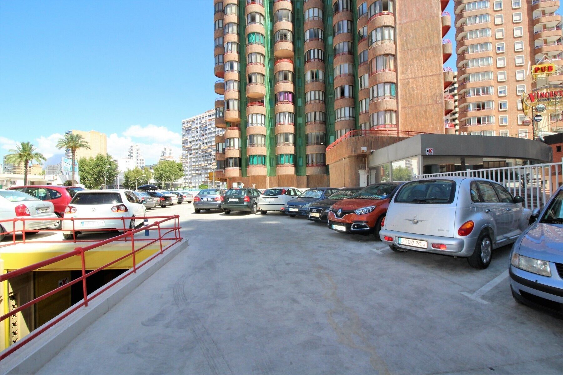 A parking lot with multiple cars, a building with balconies, and a sign for a pub.