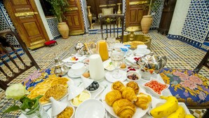 Une table de petit-déjeuner avec divers aliments et boissons, entourée d’une décoration de style marocain.