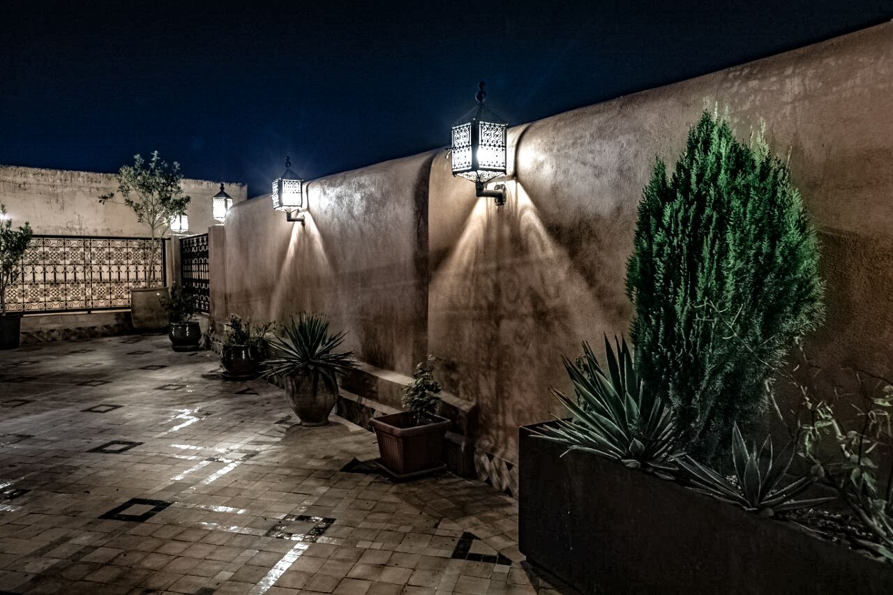 An outdoor patio area with a tiled floor, potted plants, and wall-mounted lanterns.