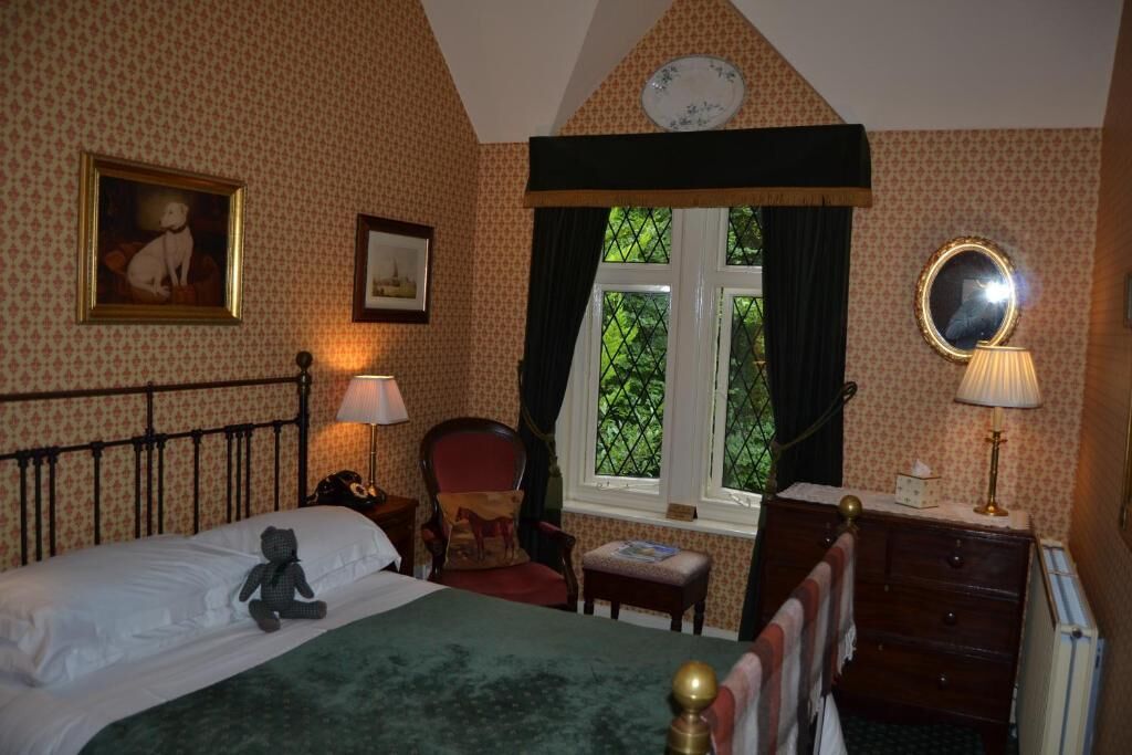 A bedroom with a bed, a chair, a dresser, a window with curtains, and a wall clock.