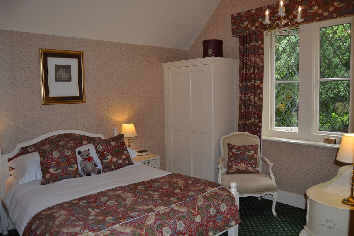 A bedroom with a bed, a chair, a wardrobe, and a window with curtains.