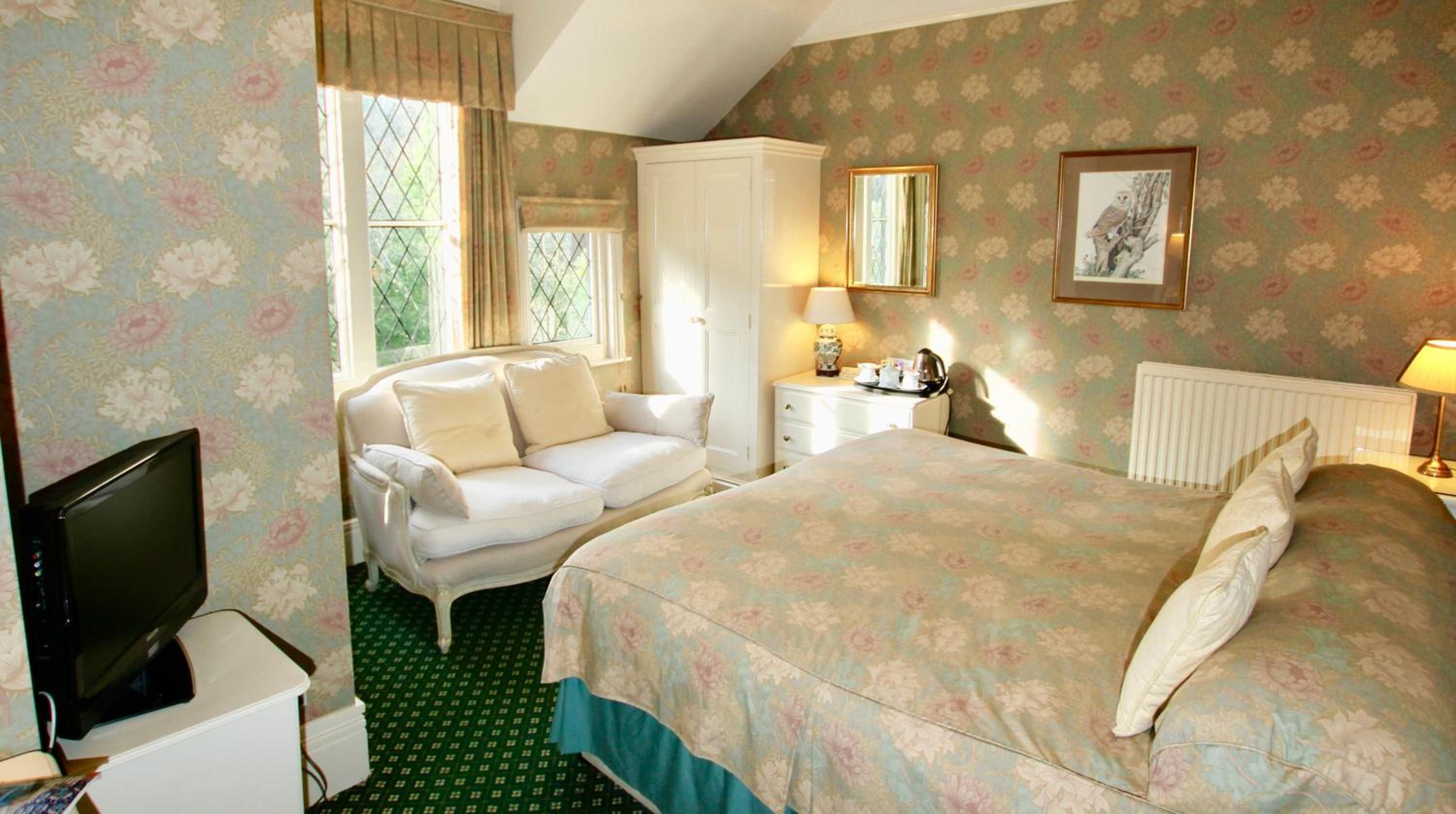 A bedroom with a bed, a sofa, a dresser, a television, and a window with curtains.