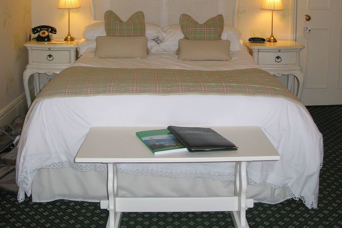 A neatly arranged bedroom with a large bed, two bedside tables with lamps, and a small table with a book and a remote control.