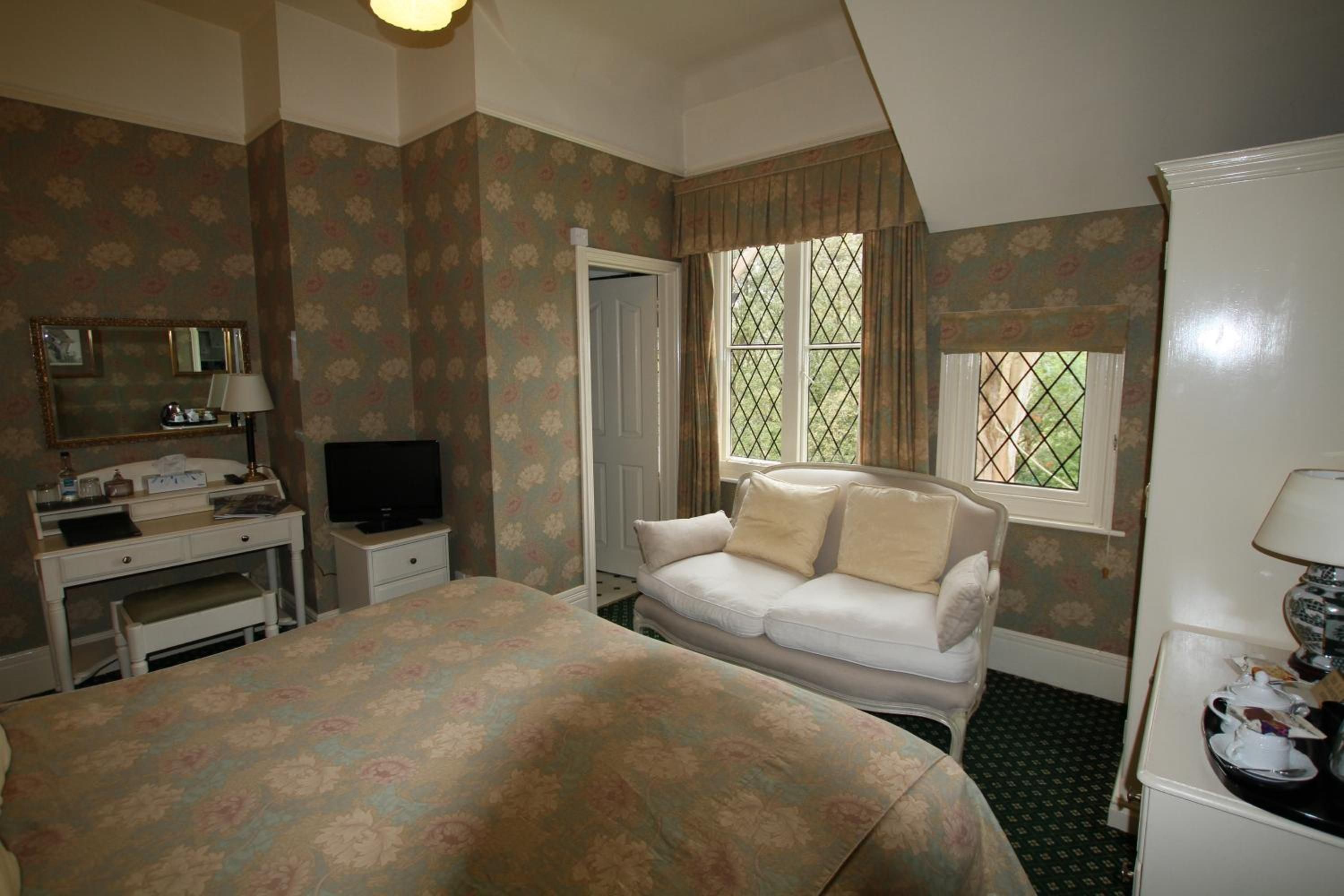 A bedroom with a bed, a desk with a television, a window with curtains, and a dresser.