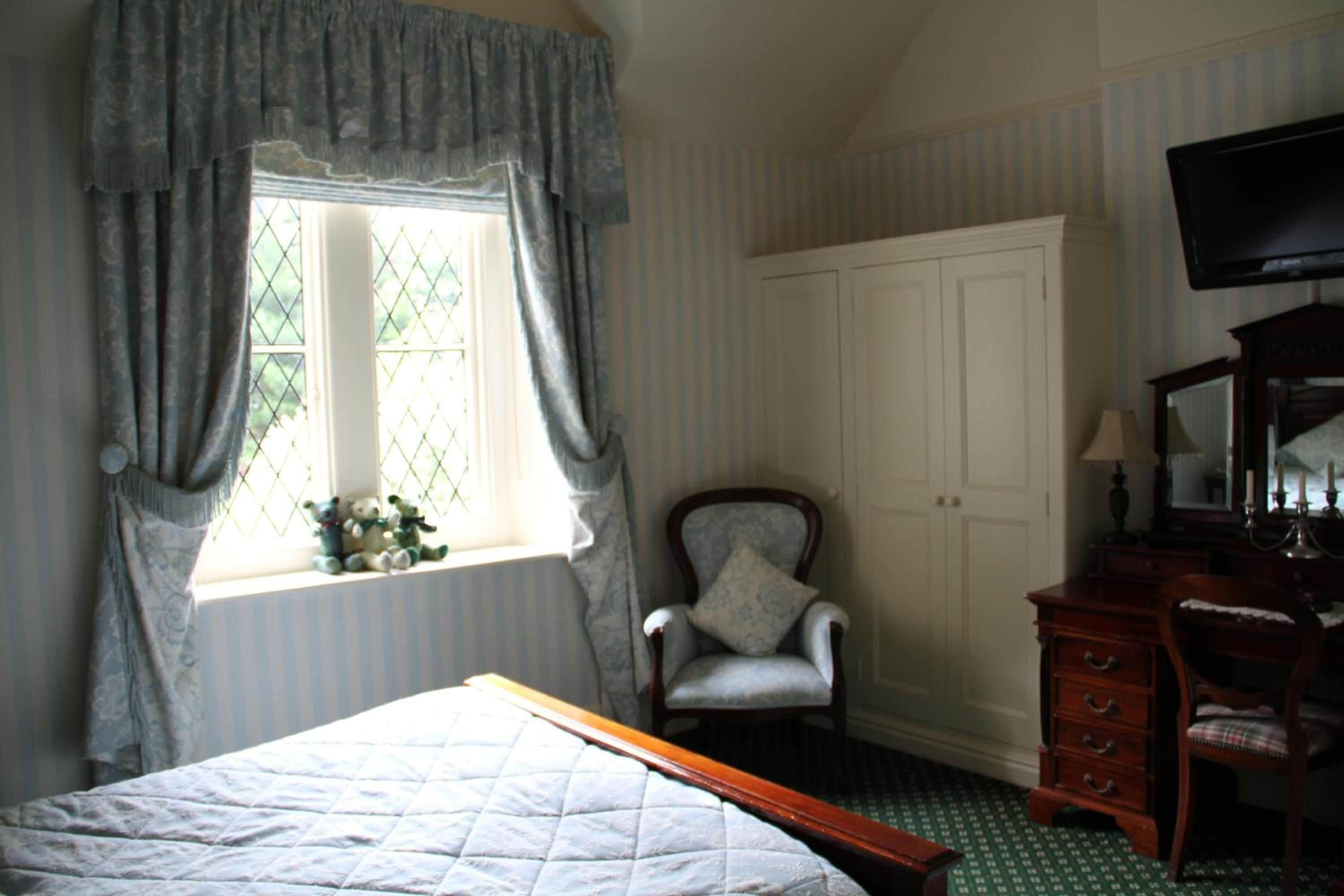 A bedroom with a bed, a chair, a dresser, a television, and a window with curtains.