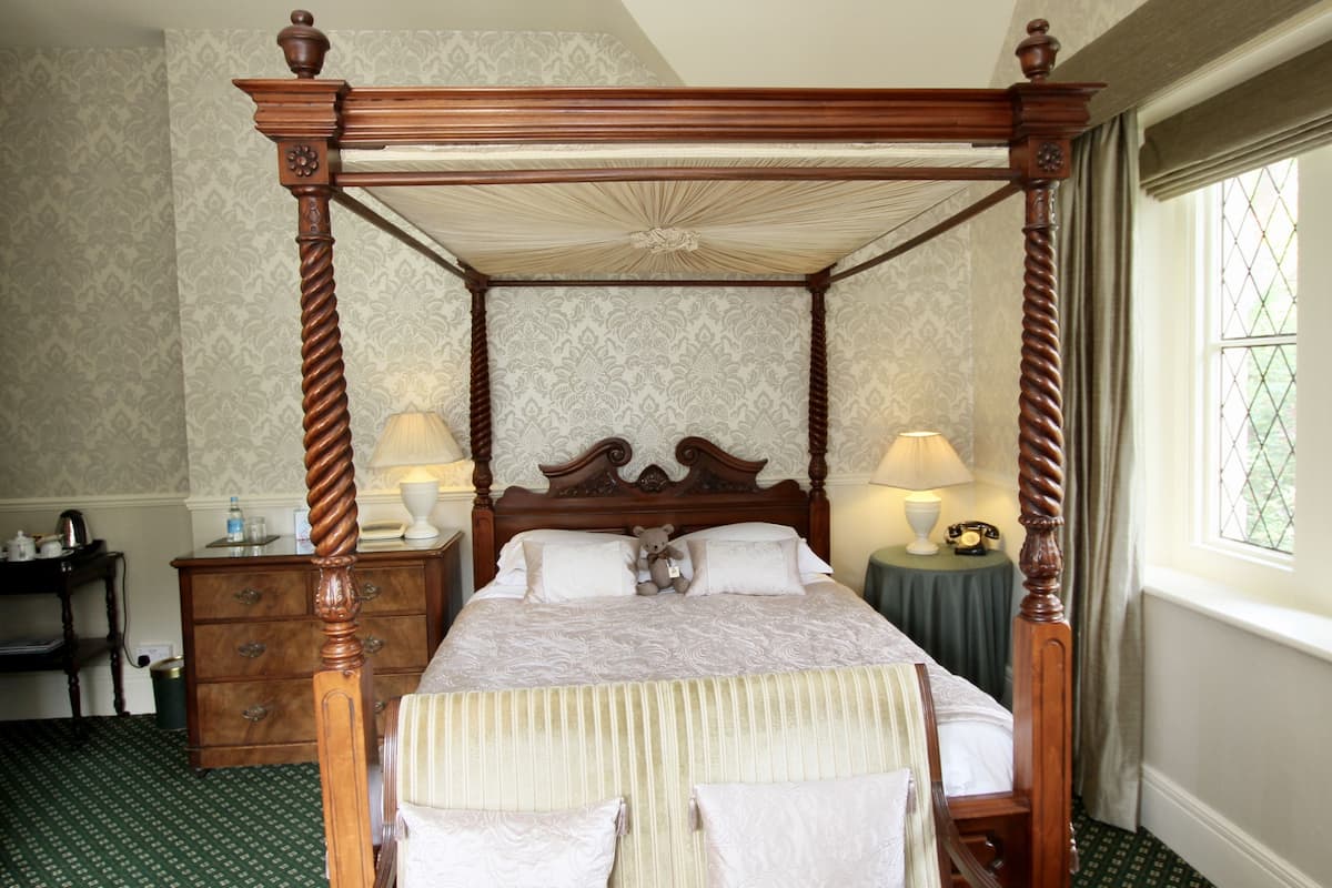 A four-poster bed with a wooden frame, a green patterned carpet, and a nightstand with a lamp.