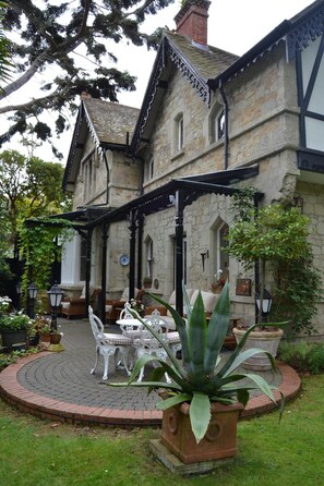 A traditional stone building with a covered patio area featuring outdoor furniture and a central plant. - Rylstone Manor (Shanklin)