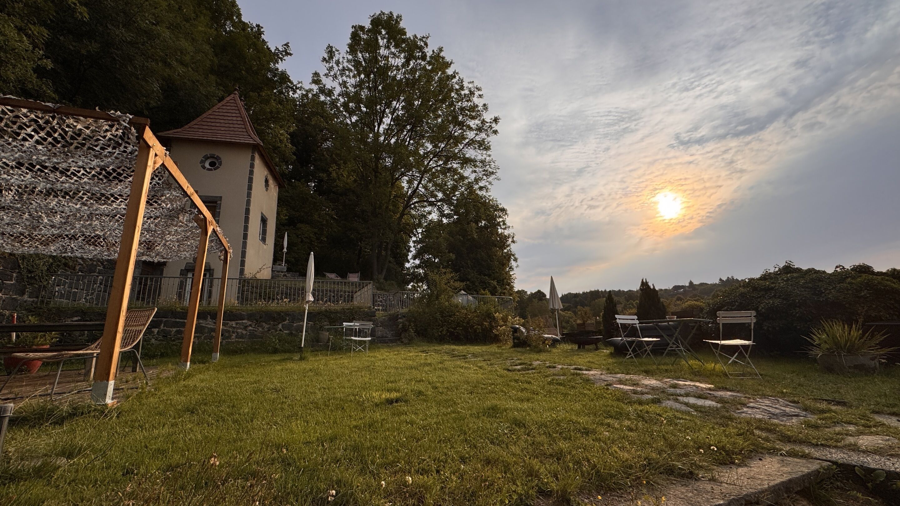 Un espace extérieur verdoyant, avec une structure en bois, un petit bâtiment et un ciel dégagé où le soleil se couche.