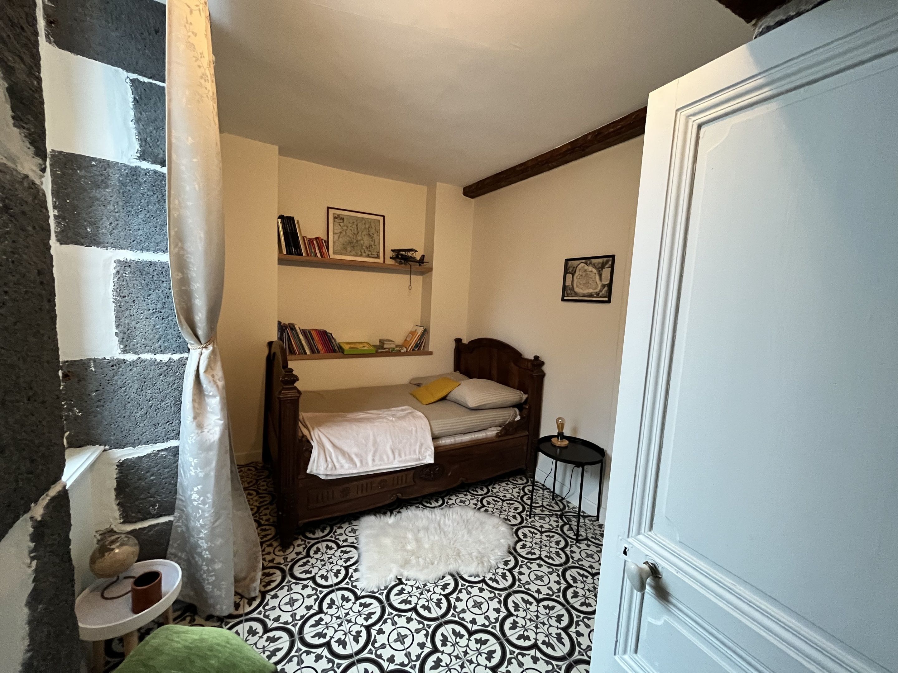 Een slaapkamer met een bed, een klein nachtkastje, een stoel, een vloer met patroon en een deur.