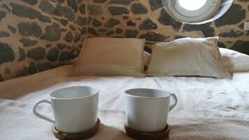 A bed with two white mugs on coasters, a stone wall, and a round window.