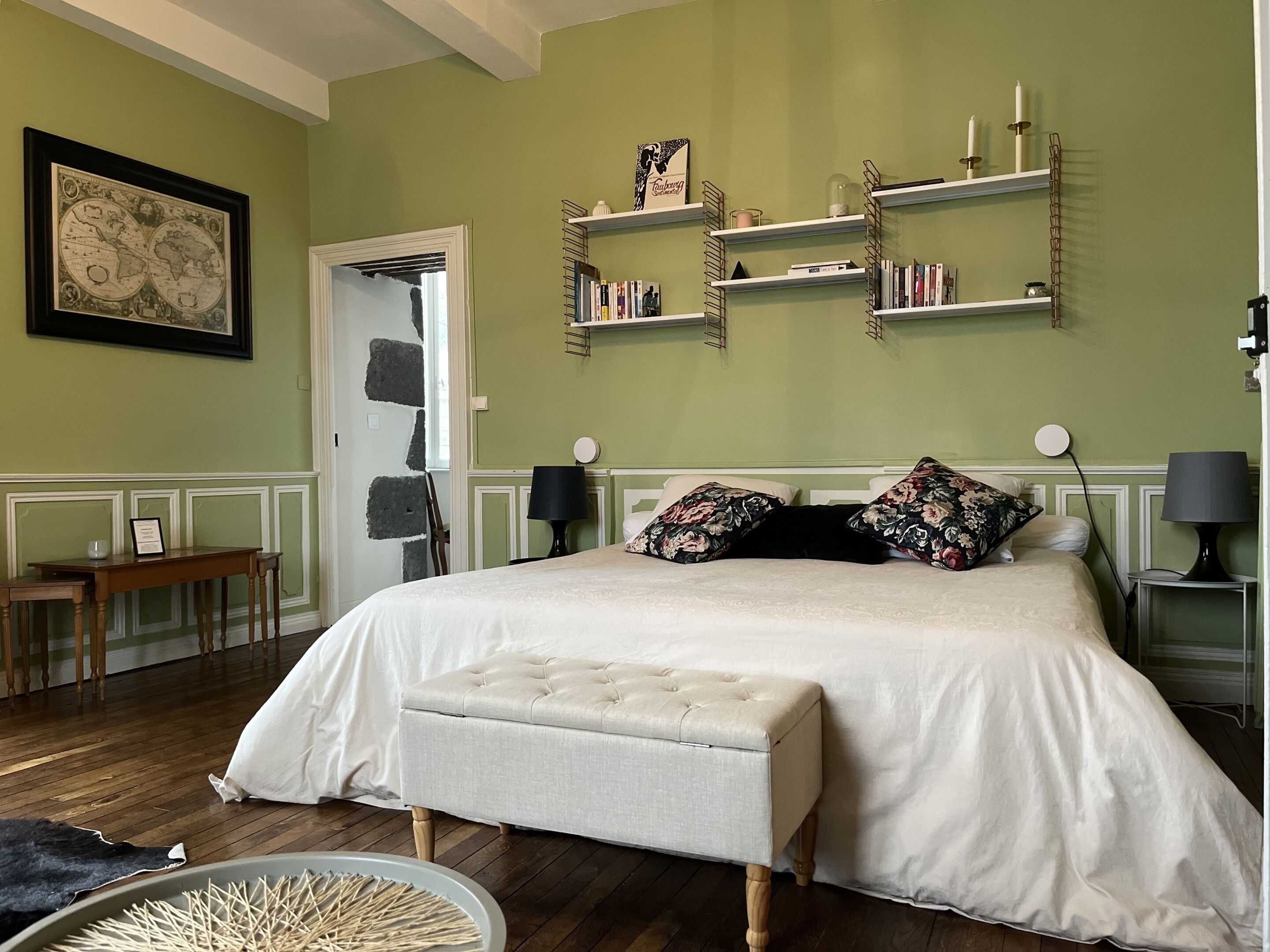Ein Schlafzimmer mit einem Bett, Nachttischen, einer Lampe, Regalen mit Büchern und einer gerahmten Weltkarte.