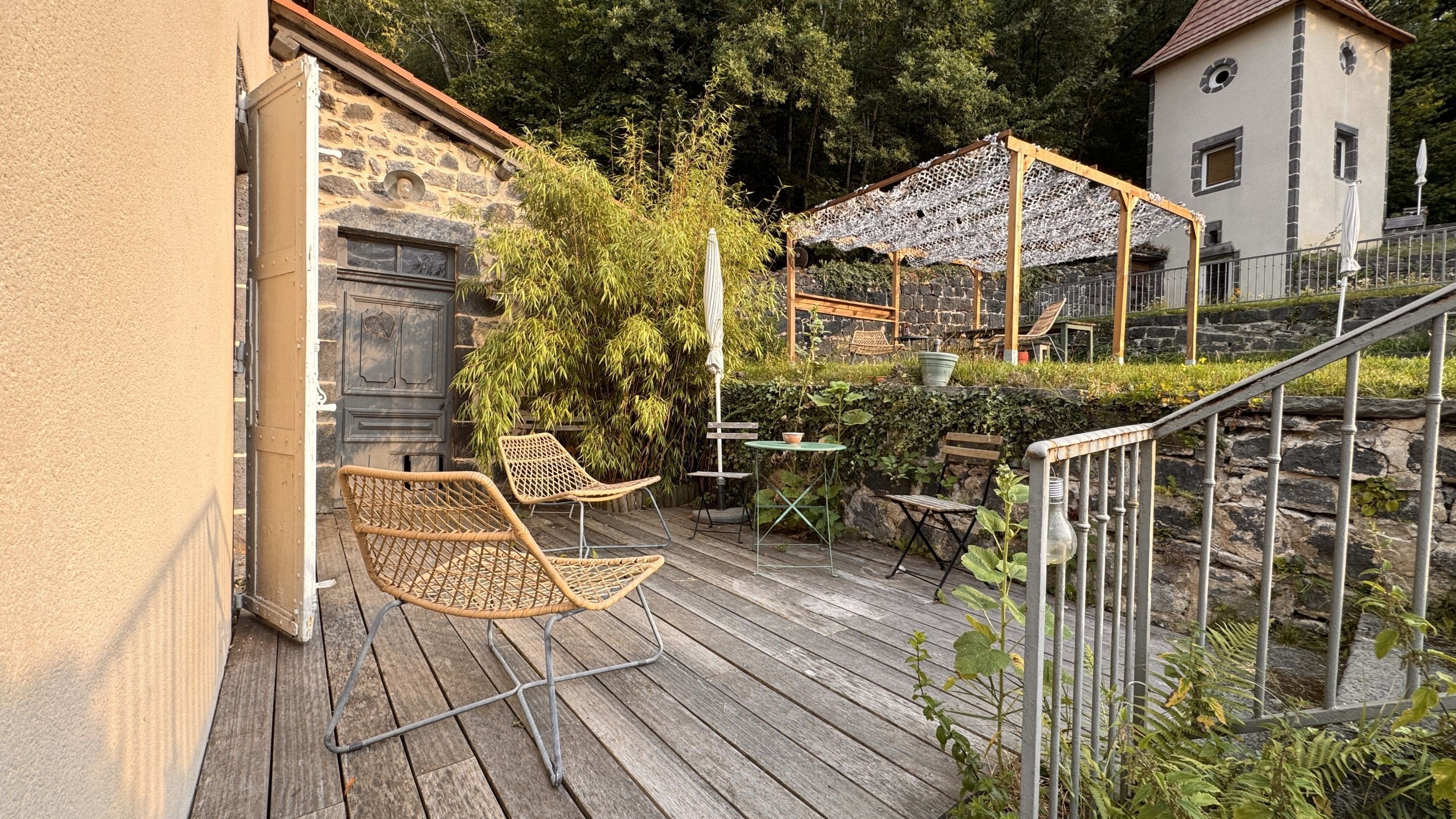 Eine Holzterrasse mit Korbstühlen, einem Tisch und einer Pergola mit Netzdach.