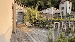 Una terraza de madera con sillas de mimbre, una mesa y una pérgola con techo de mosquitera.