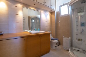 A modern bathroom with a wooden vanity, a glass shower enclosure, and a toilet. - Rhea - Glyfada Sea View Apartment (Glyfada)
