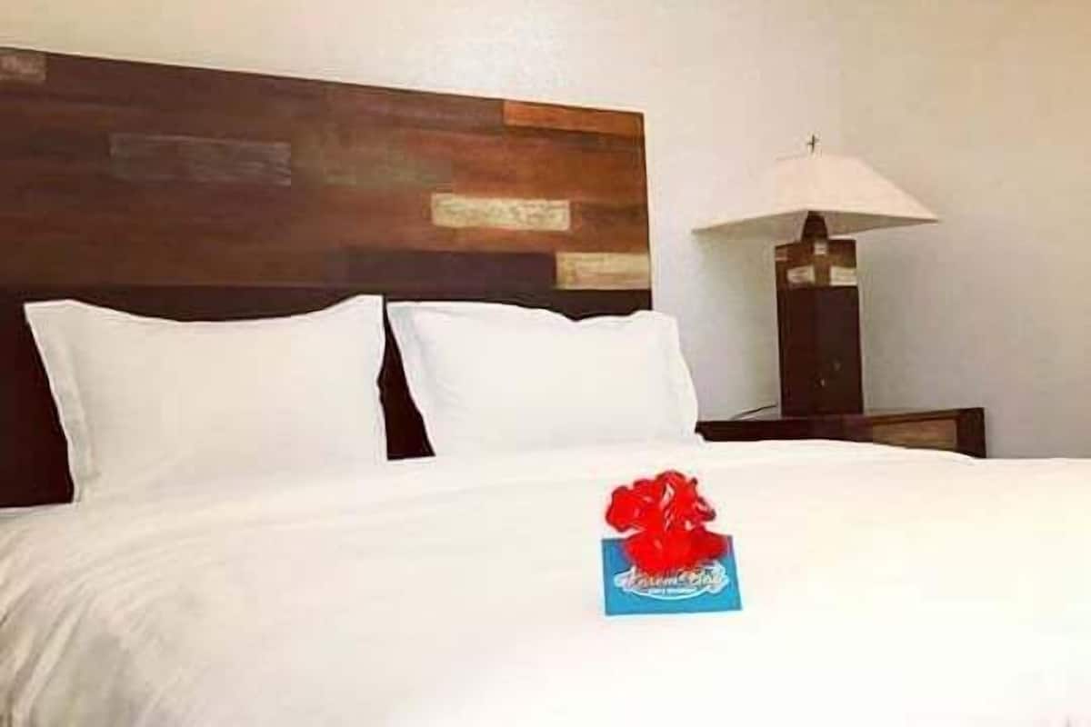 A hotel room with a large bed, a wooden headboard, a nightstand with a lamp, and a framed picture on the wall.