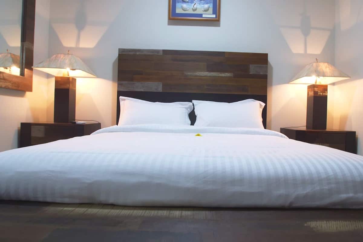A neatly made bed with white linens, a wooden headboard, and two bedside lamps on either side.