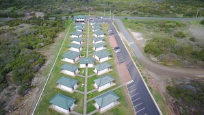 An aerial view of a resort with multiple bungalow-style accommodations arranged in rows, a parking area, and a road leading to the beach. - Hotel Karem Bay (Koumac)