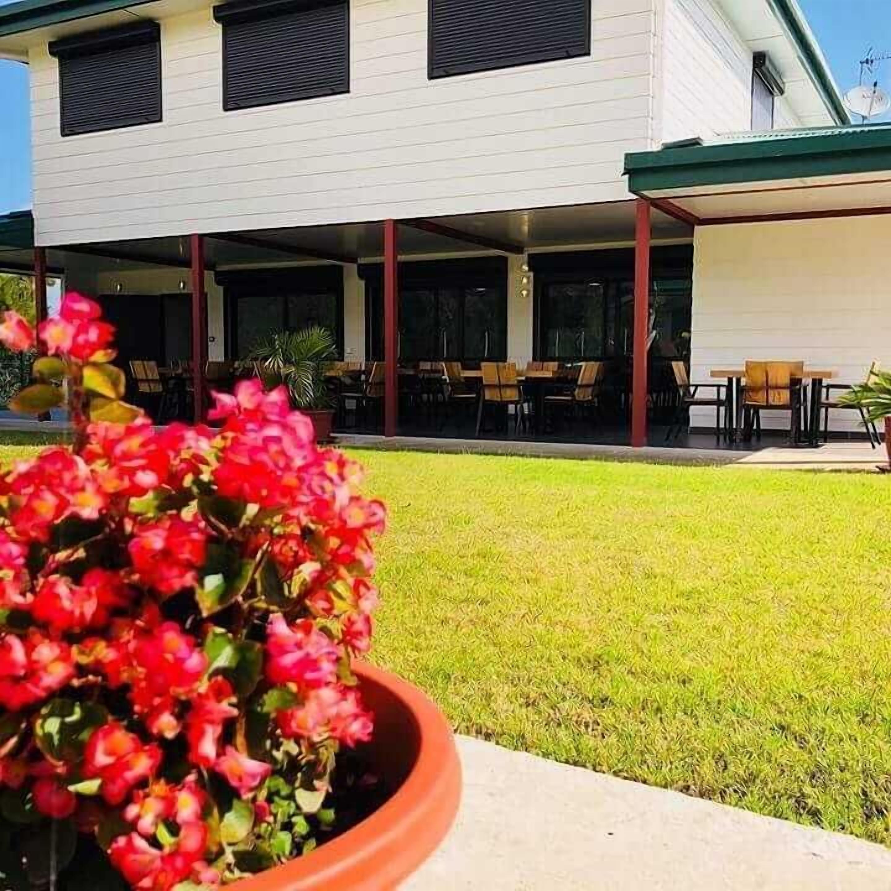 A building with a covered patio area, outdoor seating, and a potted plant with red flowers.