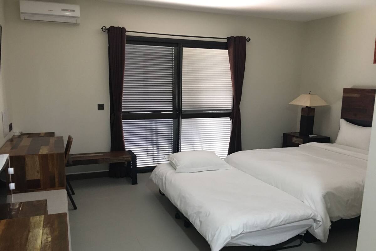 A hotel room with a bed, a desk, a chair, a lamp, and a window with curtains.