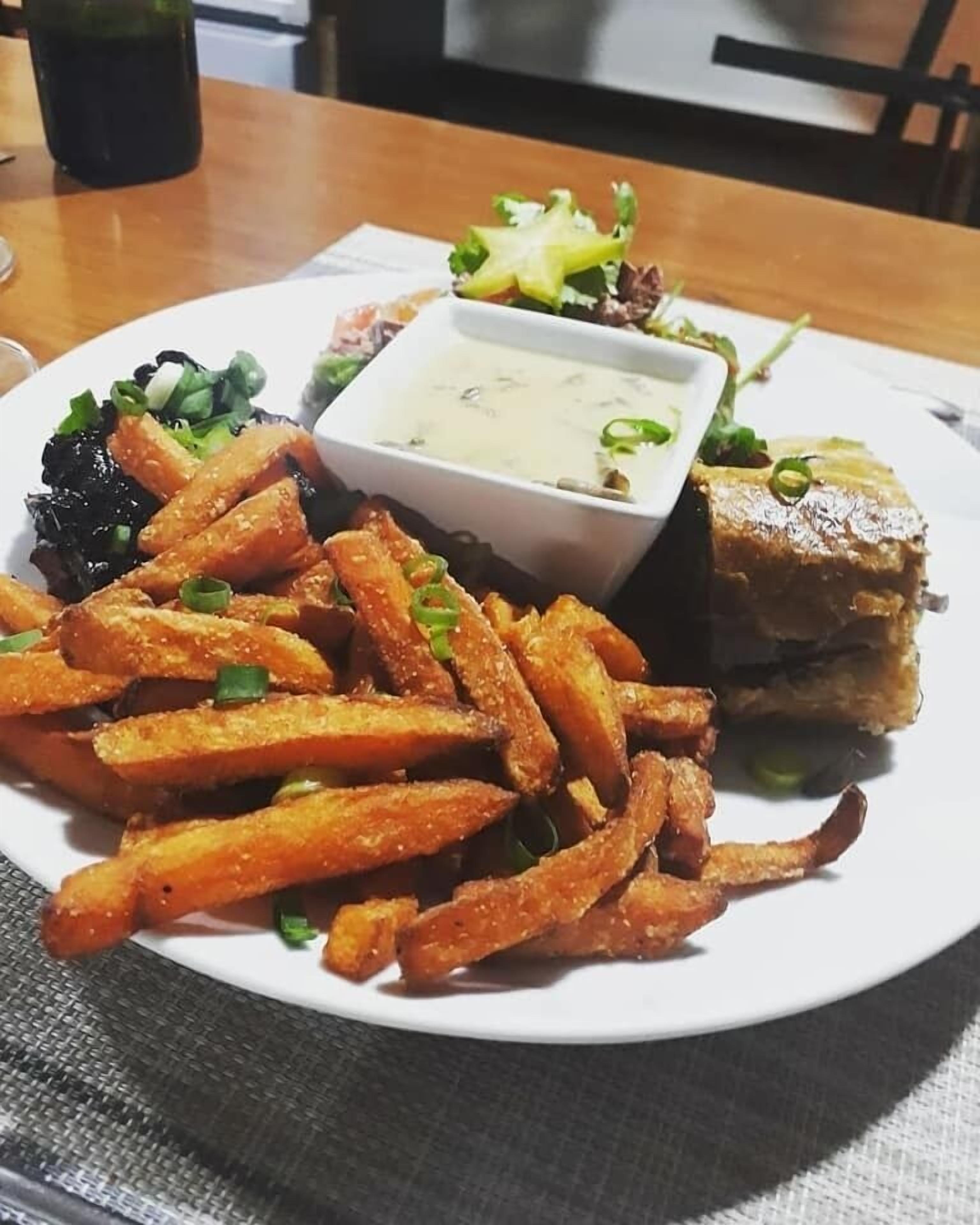 Un plato de comida con papas fritas, un trozo de carne y un recipiente pequeño de salsa.