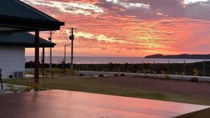 A sunset view from a covered outdoor area with a building in the foreground. - Hotel Karem Bay (Koumac)