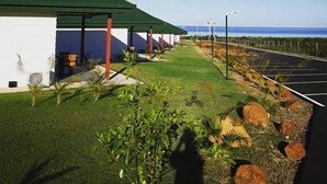 A building with a green roof and white walls, a parking area with marked spaces, and a clear view of the ocean. - Hotel Karem Bay (Koumac)
