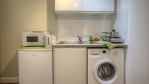 Una cocina compacta con microondas, hervidor, pileta y lavadora.