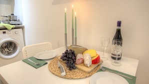 Una mesa de comedor servida con platos, cubiertos, una botella de vino y una bandeja de fruta.
