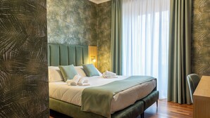 Una habitación de hotel moderna con una cama grande, un escritorio y vistas al exterior a través de cortinas traslúcidas.