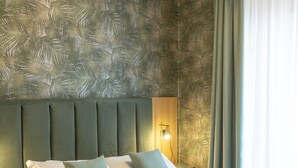 Una cama bien hecha con almohadas y toallas dobladas, un cabecero tapizado en verde y un suelo de madera.