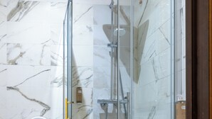 Ducha con paredes y suelo de mármol blanco, inodoro blanco y lavamanos blanco con espejo.