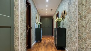 Un pasillo con papel tapiz estampado, suelo de madera y jarrones decorativos.