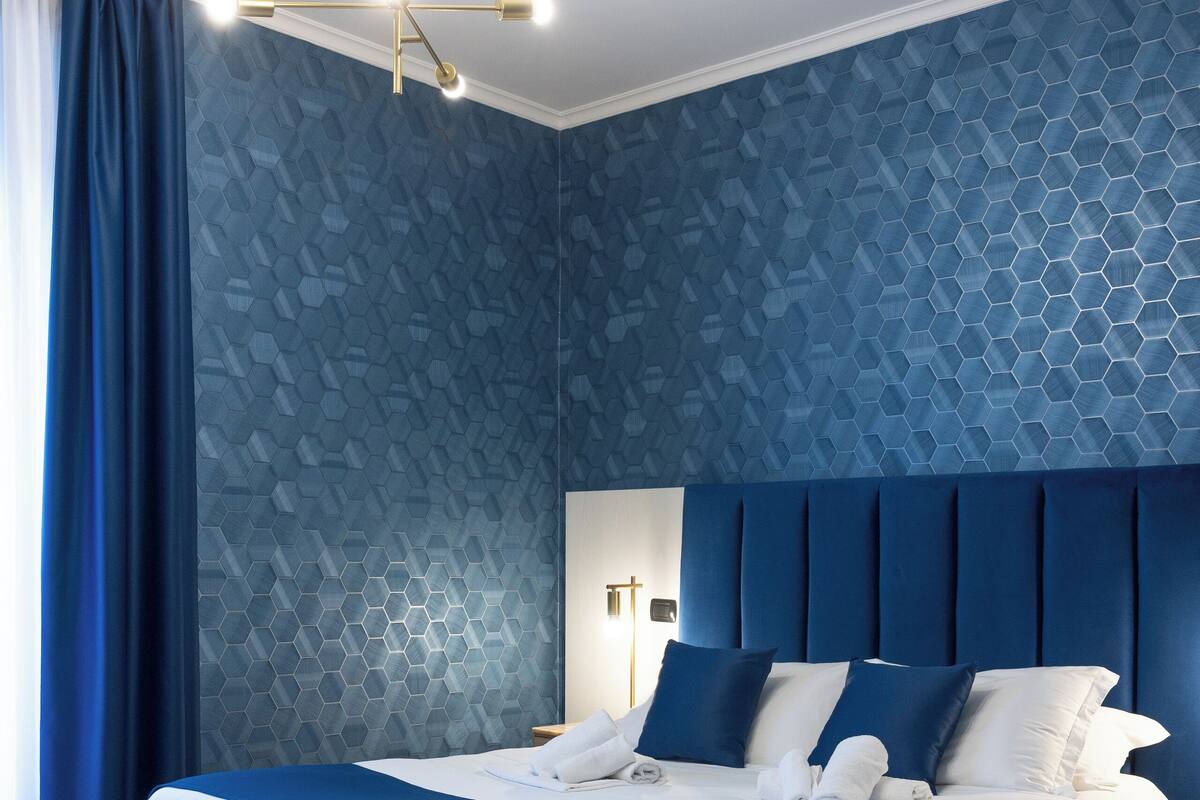A modern hotel room with a large bed, a blue upholstered chair, and a wooden floor.