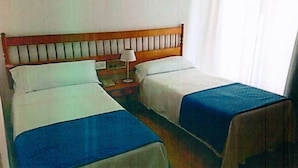 A hotel room with two single beds, a wooden headboard, a bedside table with a lamp, and a window with curtains. - Hotel Plaça Vella (Sant Carles de la Rapita)