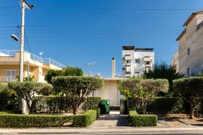 Um bairro residencial com sebes bem aparadas, um caminho pavimentado e edifícios modernos com varandas.