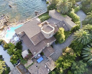 A villa with a swimming pool, terracotta-tiled roof, and lush greenery.