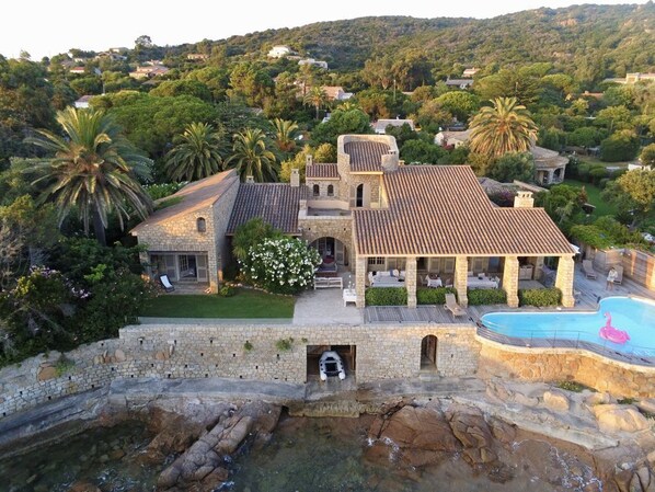 A villa with a swimming pool, stone architecture, and lush greenery.