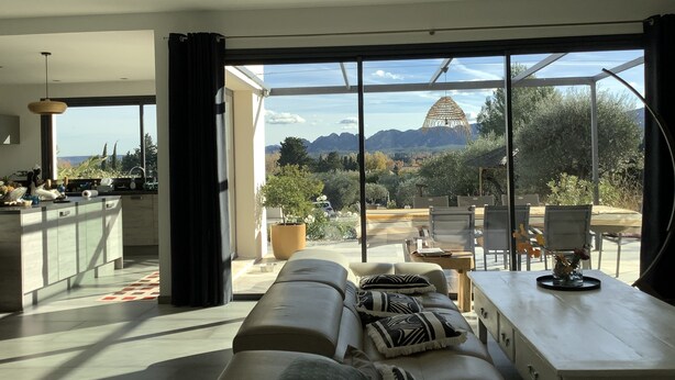 A modern living room with a sofa, a dining area, and a view of mountains through large windows. - Superb contemporary villa with private pool (Saint-Rémy-de-Provence)