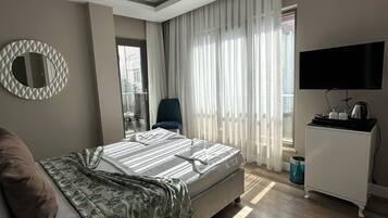 Une chambre moderne avec un lit, une télévision, un bureau et une fenêtre avec des rideaux.