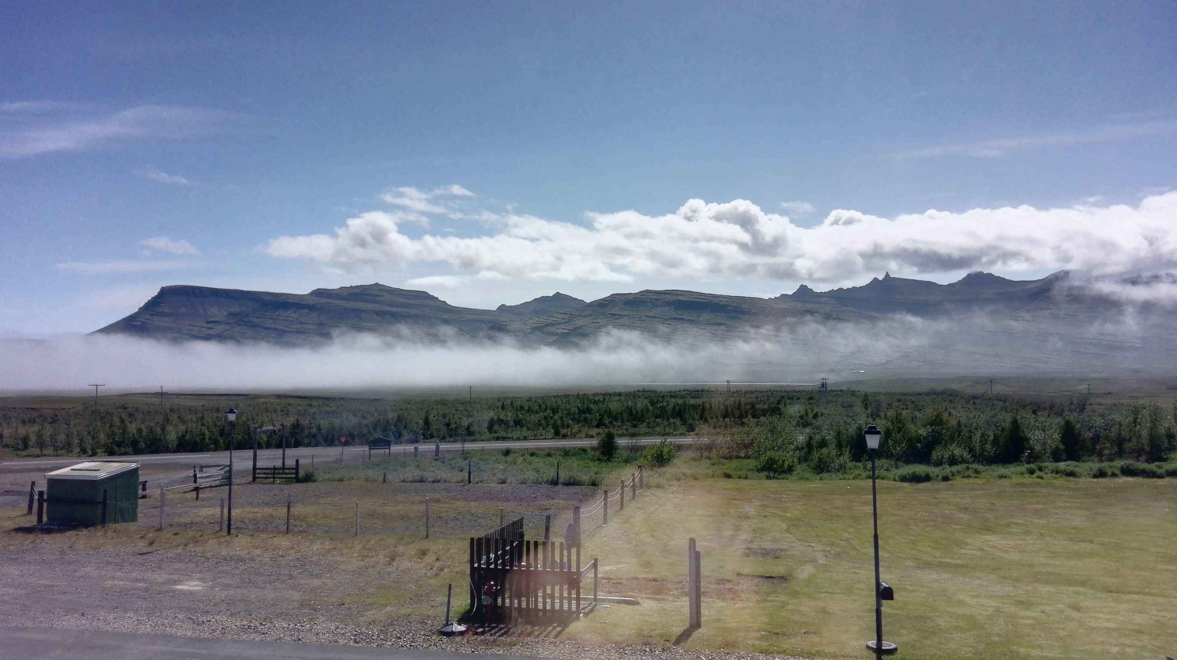 A mountainous landscape with a road leading to a gate, surrounded by greenery and a clear sky.