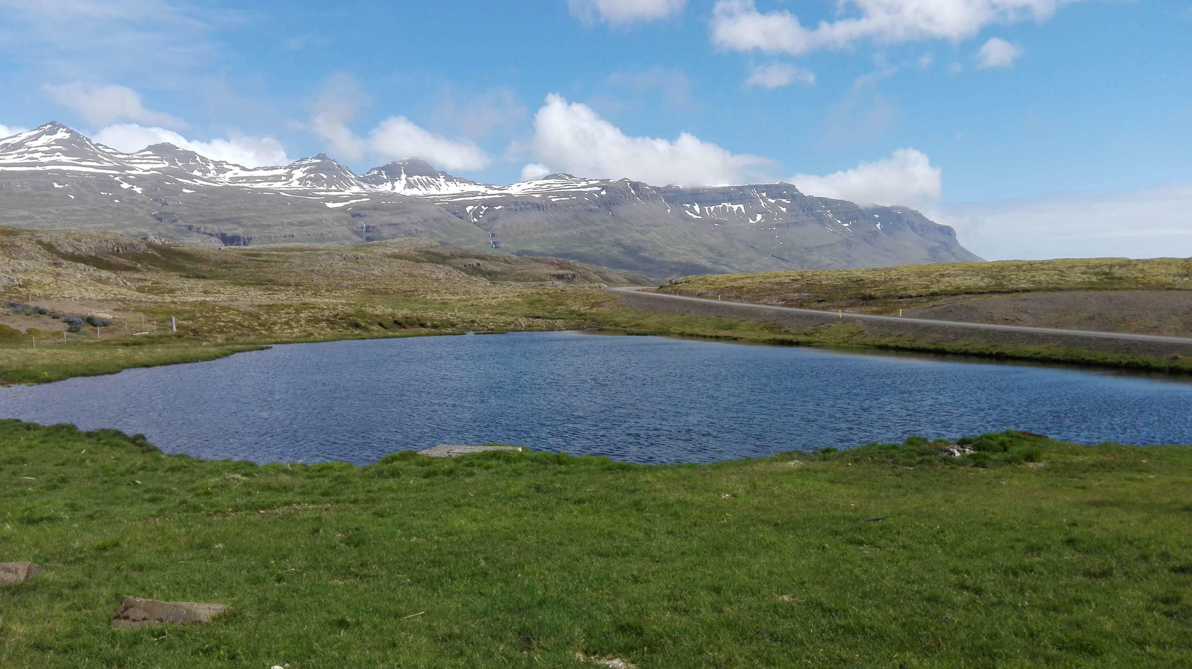 A tranquil lake with a road and mountains in the background.