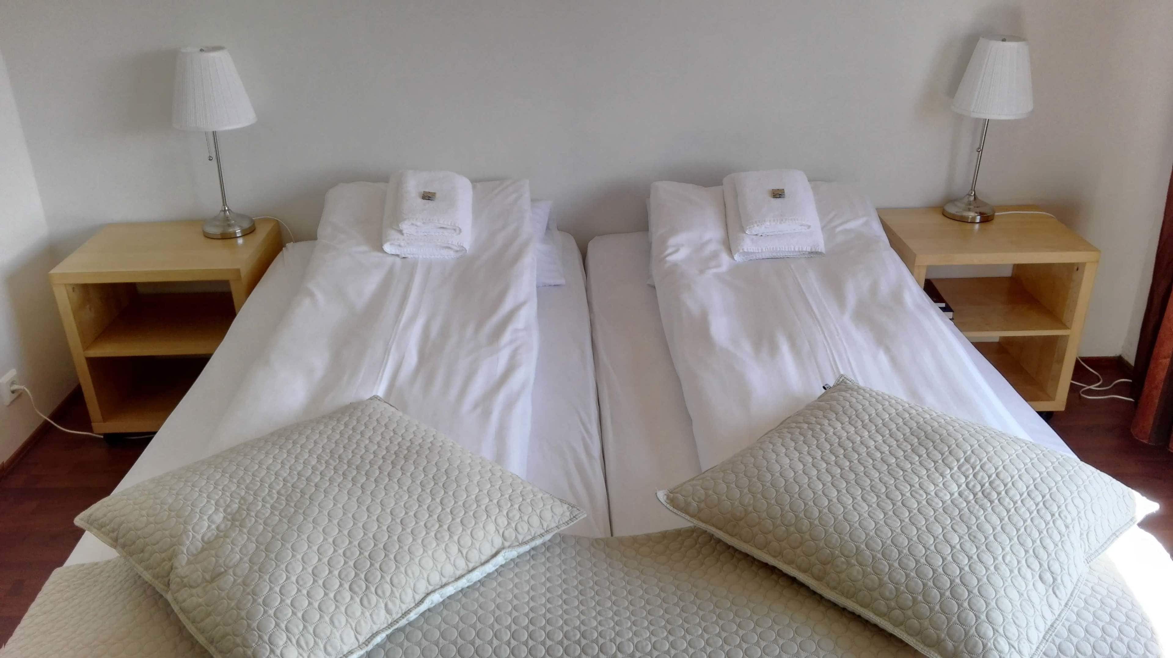 Habitación doble con dos camas, cada una con una almohada y una mesita de noche con lámpara.