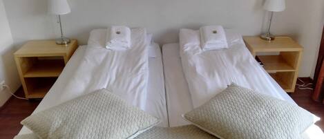 Habitación doble con dos camas, cada una con una almohada y una mesita de noche con lámpara.